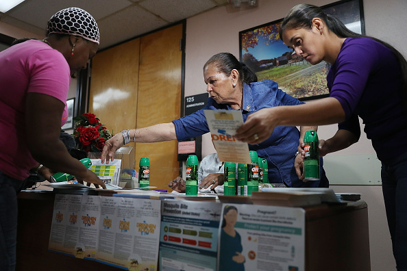 Mira Trujillo (L) picks up bug repellent from Brunilda Mendez (C) and Rachel Romano who have a table setup to help people prevent getting the Zika virus in a building located in the Wynwood neighborhood where the Zika virus has broken out on August 4 in Miami, Florida.